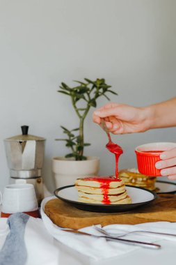 Mutfaktaki beyaz masada kahve makinesinin yanına ahududu sosu döken bir kız. Karantinada sabah kahvaltısı. Ev yapımı lezzetli krep tarifi..