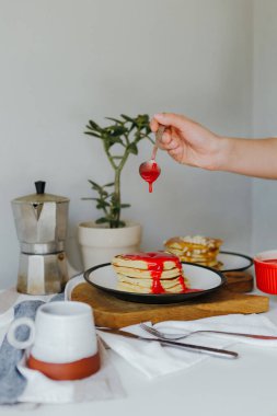 Mutfaktaki beyaz masada kahve makinesinin yanına ahududu sosu döken bir kız. Karantinada sabah kahvaltısı. Ev yapımı lezzetli krep tarifi..