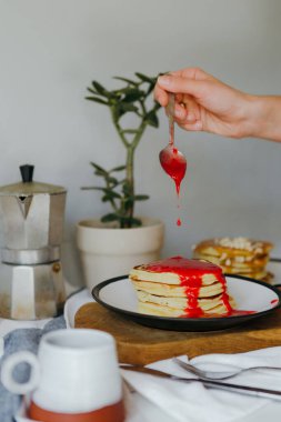 Mutfaktaki beyaz masada kahve makinesinin yanına ahududu sosu döken bir kız. Karantinada sabah kahvaltısı. Ev yapımı lezzetli krep tarifi..