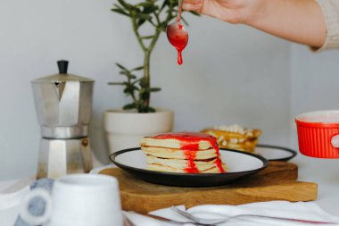 Mutfaktaki beyaz masada kahve makinesinin yanına ahududu sosu döken bir kız. Karantinada sabah kahvaltısı. Ev yapımı lezzetli krep tarifi..