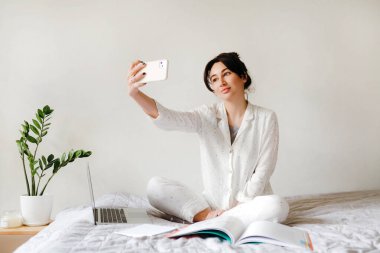Genç güzel kız evde çalışırken ve ders çalışırken selfie çekiyor. Merkez ofis. Tecrit altında çalışma kavramı.