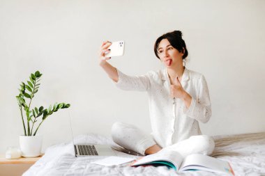 Genç güzel kız evde çalışırken ve ders çalışırken selfie çekiyor. Merkez ofis. Tecrit altında çalışma kavramı.