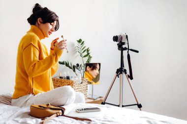 Genç esmer kız güzellik blogcusu beyaz arka planda kamera önünde cilt silindiri gösteriyor. Blog çekmenin konsepti. Güzellik ve cilt bakımı.