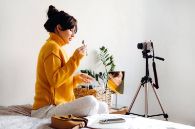 Genç esmer kız güzellik blogcusu beyaz arka planda kamera önünde cilt silindiri gösteriyor. Blog çekmenin konsepti. Güzellik ve cilt bakımı.