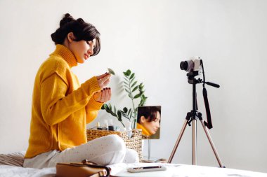Genç esmer kız güzellik blogcusu beyaz arka planda kamera önünde cilt silindiri gösteriyor. Blog çekmenin konsepti. Güzellik ve cilt bakımı.