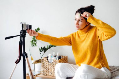 Genç esmer kız güzellik blogcusu beyaz arka plandaki odasında yüz masajı yaparken bir video blogu çekiyor. Blog çekmenin konsepti. Güzellik ve cilt bakımı.