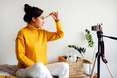 Genç esmer kız güzellik blogcusu beyaz arka plandaki odasında yüz masajı yapıyor. Blog çekmenin konsepti. Güzellik ve cilt bakımı.