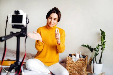 Genç esmer kız güzellik blogcusu kamerada nasıl antiseptik kullanılacağını gösteriyor. Blog çekmenin konsepti. Güzellik ve cilt bakımı.