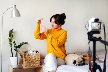 Genç esmer kız güzellik blogcusu kamerada cilt bakımı için nasıl serum yapılacağını gösteriyor. Blog çekmenin konsepti. Güzellik ve cilt bakımı.