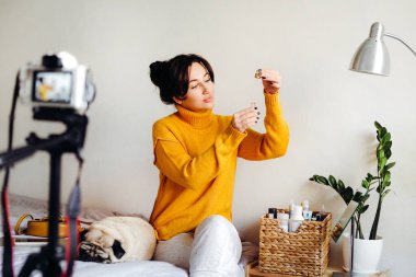 Genç esmer kız güzellik blogcusu kamerada cilt bakımı için nasıl serum yapılacağını gösteriyor. Blog çekmenin konsepti. Güzellik ve cilt bakımı.