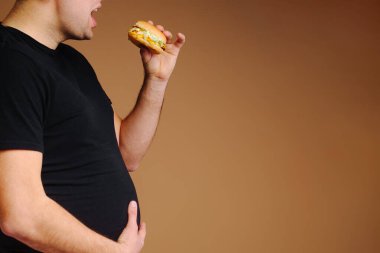 Şişman adam hamburgeri tutuyor ve karnını sıkıca tutuyor. Abur cubur yüzünden karın ağrısı. Sağlıksız.