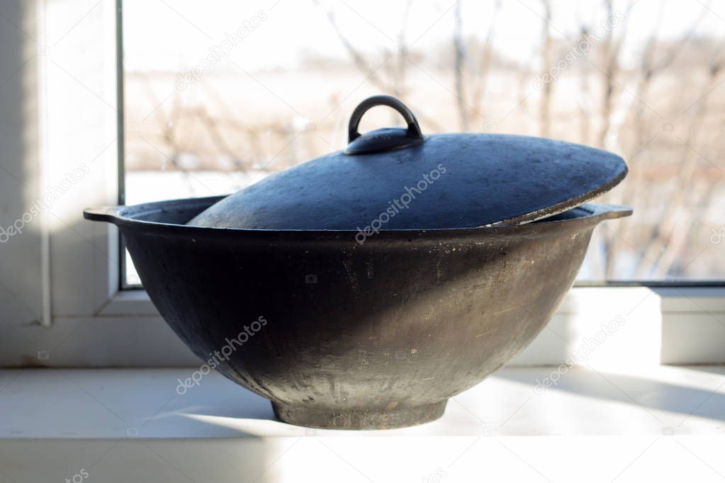 Cast iron cauldron on the windowsill. Wok for pilaf.
