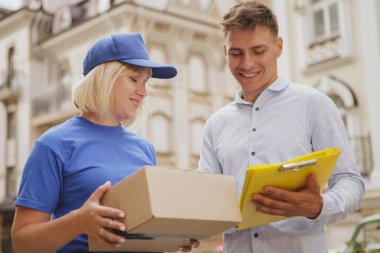 Şehir sokaklarında mavi üniformalı, dost canlısı bir teslimatçı kadın.