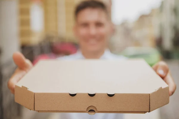 Красивый молодой человек ходит по городской улице с коробкой пиццы — стоковое фото