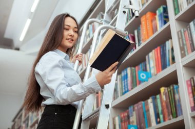 Kütüphanede kitap okuyan çekici Asyalı kadın.