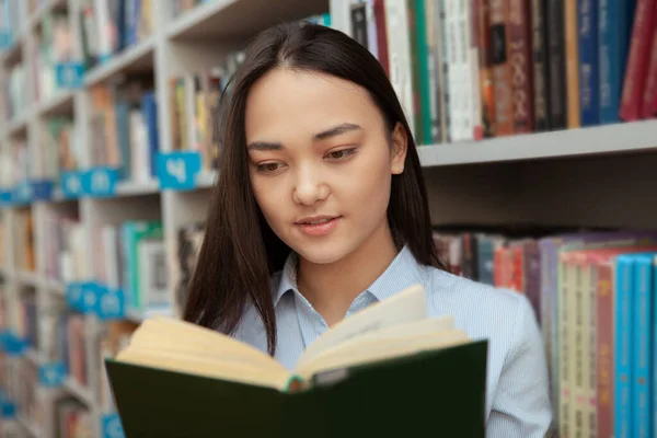 Houkutteleva aasialainen nainen lukee kirjastossa — kuvapankkivalokuva