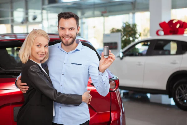 Handsome happy man hugging his lovely wife smiling to the camera with a car key in his hand, copy space. Couple celebrating buying new auto