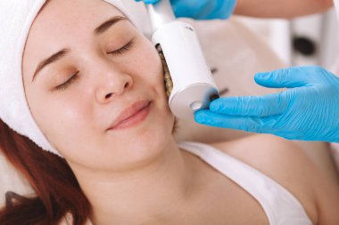 Cropped close up of a young relaxed woman smiling while getting skin tightening facial treatment by beautician. body care therapy concept