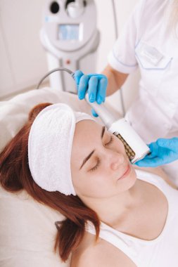 Vertical shot of a young woman receiving skin tightening  facial massage at cosmetology clinic