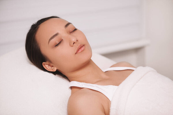 Великолепная молодая азиатка отдыхает в салоне красоты после процедуры по уходу за кожей. Красивая женщина лежит с закрытыми глазами отдыхает в спа
