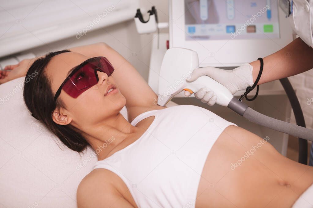 Young Asian woman getting armpit laser hair removal treatment at beauty clinic