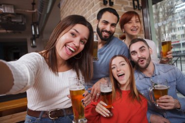 Çekici, heyecanlı kadın arkadaşlarıyla bira barında selfie çekiyor. Arkadaşlar birlikte bira içerek eğleniyorlar.