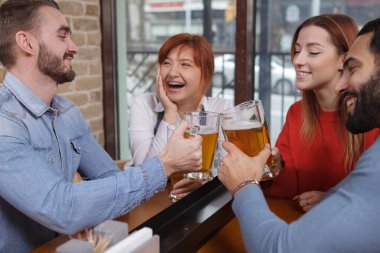 Mutlu gençler gülüyor, bardakları tokuşturuyor. Neşeli arkadaşlar birlikte bira içiyorlar.