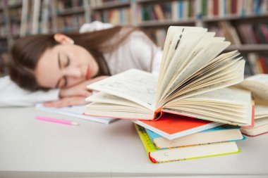 Kütüphanedeki kitap yığınına seçici odaklanma, kütüphanede okuduktan sonra çalışma kâğıtları üzerinde uyuyan genç kız.