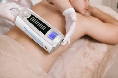 Profesyonel bir terapistin, sonosferdeki masaj cihazıyla erkek bir müşterinin sırtına masaj yaparken görüntüsü.