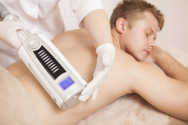 Selective focus on  massage device in the hands of cosmetologist massaging back of a male patient