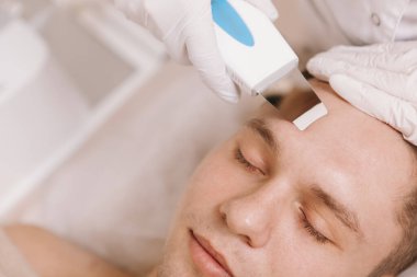 Güzellik salonunda ultrasonla deri temizleme işlemi yaptıran genç bir adamın görüntüsü.