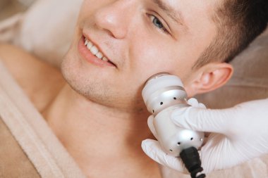 Güzellik kliniğinde yüz donanımı ameliyatı olurken gülümseyen genç bir adamın görüntüsü.