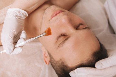 Profesyonel güzellik uzmanının taktığı yüz maskesi olan genç bir adama yaklaş.