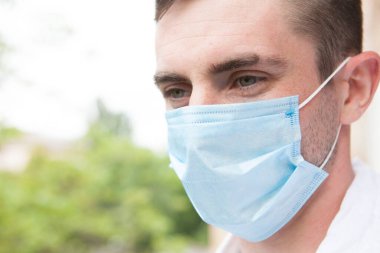 Tıbbi koruyucu maske takan, dışarıyı seyreden güzel gözlü bir adama yaklaş.