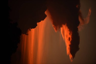 Dağın zirvesine günbatımı manzara. Turuncu-kırmızı bulutun turuncu gökyüzü ve üst üste gelen dağ manzaraları vardır.