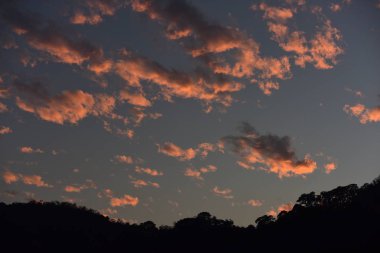 Dağlarda gün batımı. Dağların ardından yoğun bir orman alanının arkasında batan bir güneşin resmi