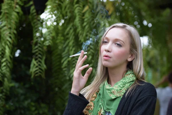 在绿色花园中吸烟的年轻女子 — 图库照片