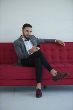 Kanepede otururken akıllı telefon kullanan zarif bir adam.