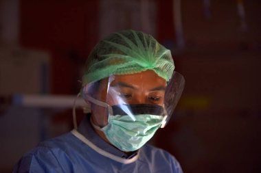 Koruyucu maskeli ve üniformalı bir erkek doktor hastanede çalışıyor.