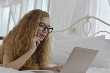 Avrupalı bir kadın yatakta dizüstü bilgisayar kullanıyor.