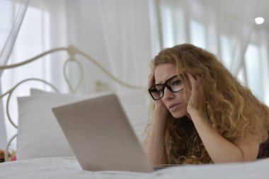 Avrupalı bir kadın yatakta dizüstü bilgisayar kullanıyor.