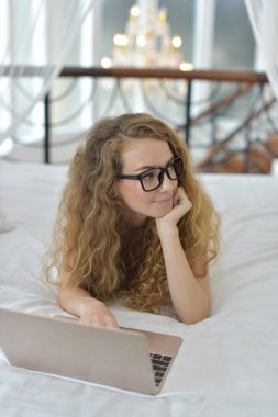 Avrupalı bir kadın yatakta dizüstü bilgisayar kullanıyor.