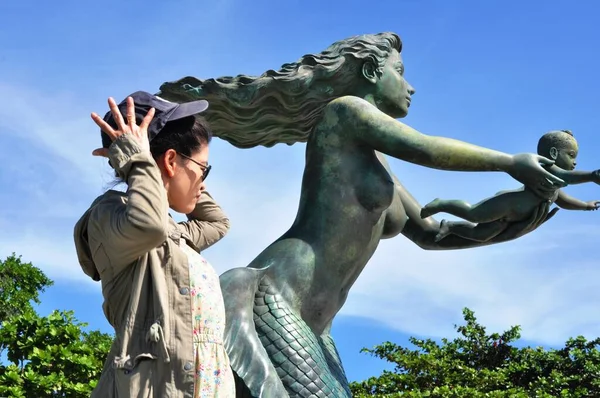 Woman near sculpture of mermaid with child on sea coast
