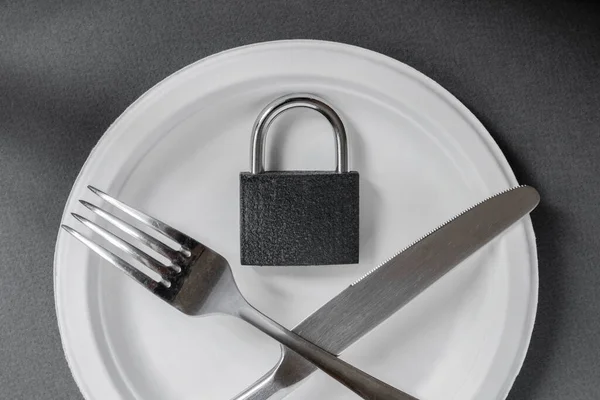 Çapraz metal bıçak ve çatal, kapalı kilit boş bir tabakta yatıyor. Gri arka planda beyaz bir plaka. Bulimia ve anarex.