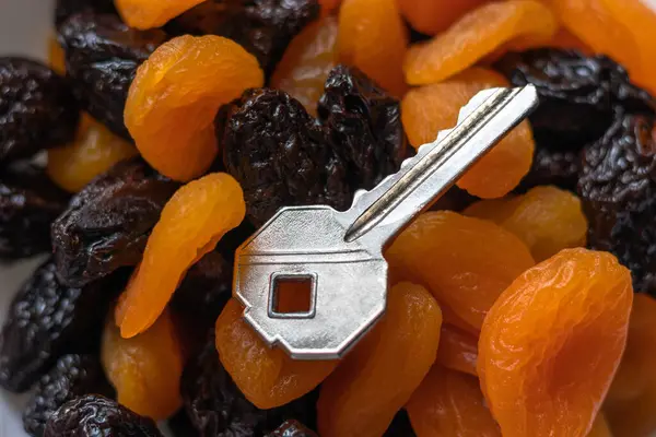 Lezzetli turuncu kurutulmuş kayısı ve koyu kahverengi kuru erik yığınının üzerinde metal bir anahtar. Kabızlığa karşı bir çare..