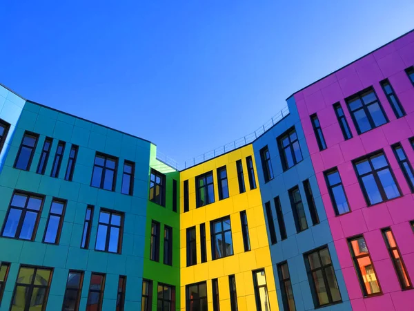 Multi-colored facades of the school with black window frames. Look up from the blue sky