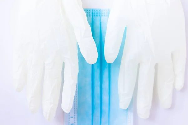 Tıbbi tek kullanımlık mavi maske ve beyaz arka planda duran bir çift beyaz lateks eldiven. Bir doktor ya da virüslü basit bir insan için gerekli koruyucu ekipman. Kavram. Covid-19, koronavirüs..