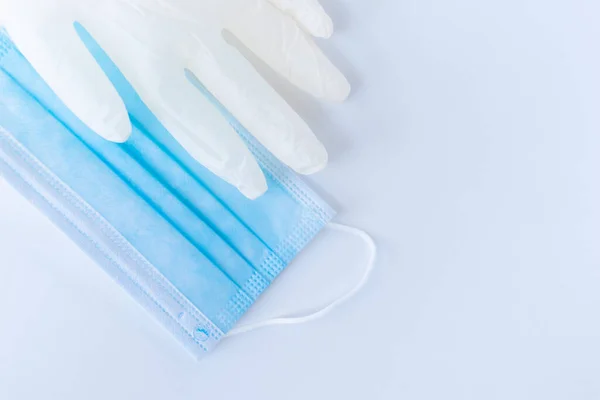 Tıbbi tek kullanımlık mavi maske ve beyaz arka planda duran beyaz lateks eldivenlerden biri. Bir doktor ya da virüslü basit bir insan için gerekli koruyucu ekipman. Kavram. Covid-19, koronavirüs..