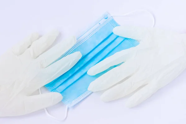 Tıbbi tek kullanımlık mavi maske ve beyaz arka planda duran bir çift beyaz lateks eldiven. Bir doktor ya da virüslü basit bir insan için gerekli koruyucu ekipman. Kavram. Covid-19, koronavirüs..