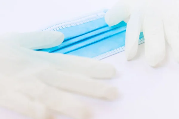 Medical disposable blue mask and a pair of white latex gloves lie on a white background. Necessary protective equipment for a doctor or a simple person from viruses. Concept. Covid-19, coronavirus.